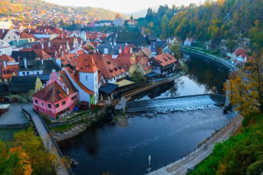 Sakin bir nehir ve ormanlık tepelerle çevrili küçük bir baraj ile kırmızı çatıları olan renkli tarihi şehir manzarası..