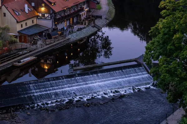 Geleneksel Avrupa evleri ve sakin sulardaki yansımalarla çağlayan nehir suyunun oluşturduğu alacakaranlık sahnesi.