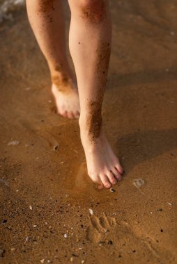 Kadın bacakları sahilde koşuyor. Islak kumda koşan bacakların yakın çekimi. Fotoğraftaki ayak izleri. Deniz sörfçüsü kız kaçıyor. Fotoğrafın dikey oryantasyonu var. Çalışan bacakların yakın plan görüntüsü