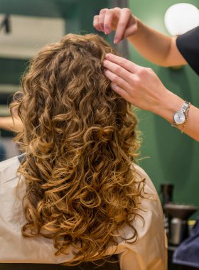 Harika bir saç modelinden sonra güzellik salonunda bir kız. Saç yakından gösteriliyor, müşteri arkadan görülüyor. Büyük dalgalı bukleler. Usta müşterileri ayarlar. Elleriyle kıvırır.