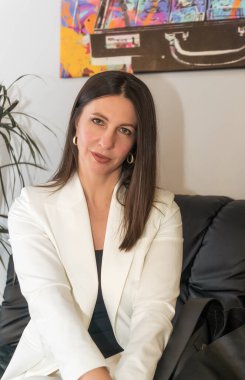 Kollarını kavuşturup kameraya bakan olgun bir iş kadınının portresi. Elinde beyaz bir miğfer var..