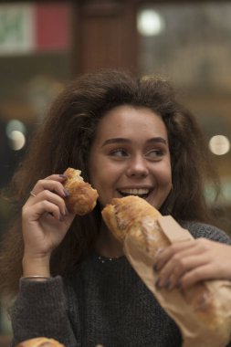 Genç kız iştahla baget yer. Ellerinde bir parça ekmek var. Dalgalı kabarık saçları var. Baget ekmeği masanın üstünde. Yüzüne yakın çekim.. 
