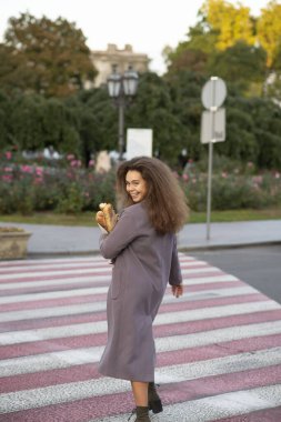 Bir kız elinde bir baget tutuyor, yaya geçidi boyunca yürüyor ve kameraya bakıyor. O, ceketli genç bir öğrenci. Saçları çok kabarık.