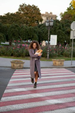 Kız elinde bir baget tutuyor ve şehirde yürüyor, karşıdan karşıya geçiyor. O, ceketli genç bir öğrencidir. Saçları çok kabarık..