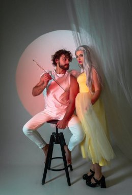 Yanında melek gibi giyinmiş bir adam duruyor. Genç adamın beyaz kanatları var. Aşıklar ve birbirlerine bakıyorlar, Sevgililer Günü için fotoğraf, aşk okunu elinde tutan adam.