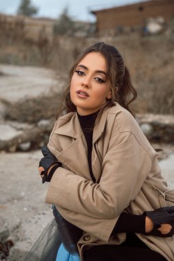 Kayaların etrafındaki deniz kıyısında genç bir kız. Bej renkli bir trençkot giymiş, deniz kıyısında kasımpatı çiçekleri arasında rüya görüyor. Mavi kumaşla süslenmiş bir sandalye.