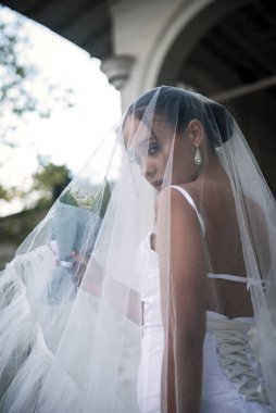 Duvakla kaplı güzel gelin. Güzel bir kız ışık inşaatının arka planında duruyor. Peçeden bakıyor, ensesinde yaka var, sırtı çıplak.