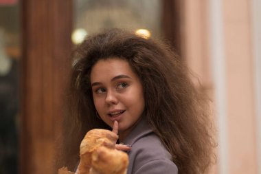 Sokakta ekmek yiyen güzel genç bir kadın. Bir kafede elinde baget ekmeği var, hem de üç tane. Gülümsüyor. Onun kabarık saçları var. Tarafsız gri kıyafetler giyiyor.