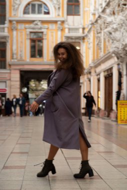 Paltolu güzel bir kız şehirde dolaşıyor. Koyu gri bir ceket ve çizme giyiyor. O, hayatla mutlu, gülüyor ve dans ediyor. Onun kabarık saçları var..