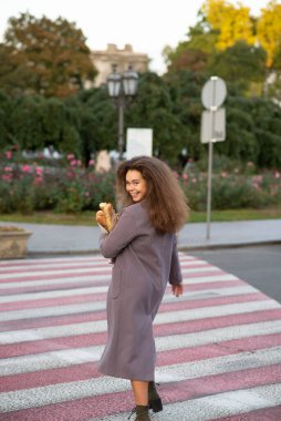 Bir kız elinde bir baget tutuyor, yaya geçidi boyunca yürüyor ve kameraya bakıyor. O, ceketli genç bir öğrenci. Saçları çok kabarık.