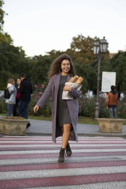 Kız elinde üç baget tutuyordu. O bir öğrenci, genç ve zayıf. Kameraya bakıyor, güzel bir gülümsemesi var. O bir ceket ve bot giyiyor..