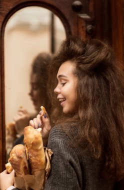 Masada oturup donut yiyen biri. Güzel bir kızın Fransız ekmeği vardır. Yumuşak ekmek yiyor ve hayattan zevk alıyor. Palto giyiyor, kıvırcık saçları var. Tahta bir masada oturuyor.