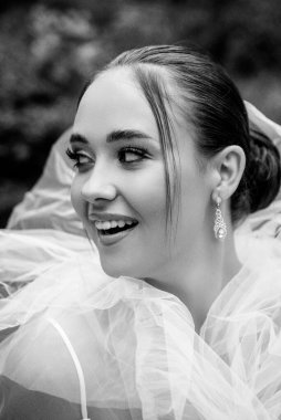 Beyaz peçeyle kaplanmış gelinin yakın çekimi. Güzel esmer kız, pürüzsüz saçları ve şık makyajı var. Kızların yüzünü saran zarif beyaz peçeler, siyah beyaz fotoğrafçılık.