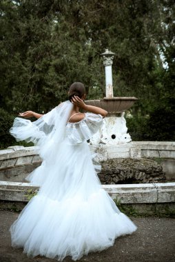 Ağaçların ve eski çeşmelerin arka planında uzun peçeli güzel bir gelin. Uzun beyaz tüylü elbiseli esmer kız gülümsüyor ve seviniyor. Gelin döner, duvak çırpınır, arkadaki eski harap çeşme