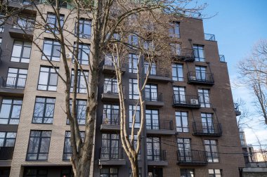 Yüksek bir bina. Yüksek kalite fotoğraf, çok katlı, enerji tasarrufu yüzlü yeni ev. Açık çizgili kahverengi duvar. Evin önünde sonbahar ağaçları.