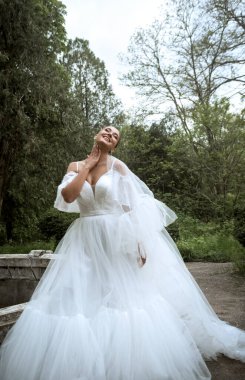 Ağaçların ve eski çeşmelerin arka planında uzun peçeli güzel bir gelin. Uzun beyaz tüylü elbiseli esmer kız gülümsüyor ve seviniyor. Duvak rüzgarda sallanıyor, gelin gökyüzüne bakıyor