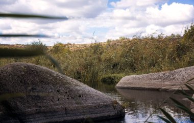 Kaya şekilli güzel mavi göl. Dağ vadisinde bir göl var, etrafında sazlıklar yetişiyor. Sudan çıkan muhteşem granit gri kayalar, yakın plan. Aktovsky Kanyonu, Ukrayna.