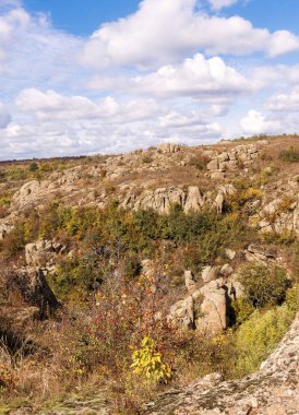Bir dağ kanyonunda antastik sonbahar, büyük kayalar. Büyük gri granit kayalar. Sarı ve kırmızı ağaçlar kayaların arasında yetişir. Aktovsky Kanyonu, taşlı Ukrayna. resimsi gökyüzü kalın bulutlu