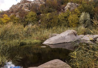 Kaya şekilli güzel mavi göl. Dağ vadisinde bir göl var, etrafında ağaçlar ve sazlıklar yetişiyor. Muhteşem gri granit kayalar sudan fırlıyor. Aktovsky Kanyonu, Ukrayna.