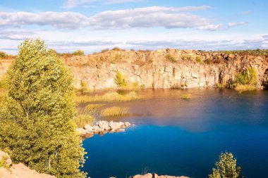 fantastic autumn in a mountain canyon. huge granite boulders around a huge bright blue lake, the lake and rocks are illuminated by the sun. Aktovsky canyon in Ukraine with cliffs.  clipart