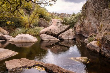 Kaya şekilli güzel mavi göl. Dağ vadisinde bir göl var, etrafında ağaçlar ve çalılar yetişiyor. Muhteşem gri granit kayalar sudan fırlıyor. Aktovsky Kanyonu, Ukrayna.