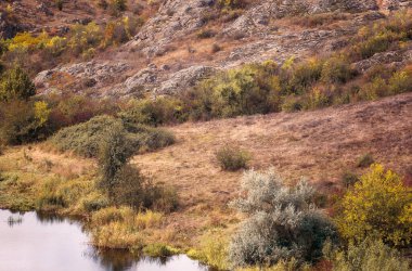 Dağ kanyonunda harika bir sonbahar. Kocaman granit kayalar. Ukrayna 'daki Aktovsky Kanyonu' nda kayalıkları, ormanları ve çayırları olan bir dağ gölü var. Parlak sarı ağaçlar, gölün etrafındaki çayırlar.