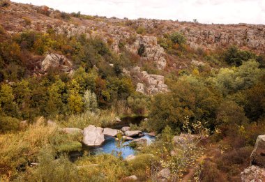 Fantastic autumn in a mountain canyon. Huge granite boulders. Aktovsky canyon in Ukraine with cliffs, picturesque forests and meadows, a large mountain lake below. Bright yellow and red trees. clipart