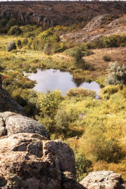 Dağ kanyonunda harika bir sonbahar. Kocaman granit kayalar. Ukrayna 'daki Aktovsky Kanyonu' nda kayalıkları, ormanları ve çayırları var. Aşağıda parlak mavi bir dağ gölü var. Göl çayırının etrafındaki parlak sarı ağaçlar