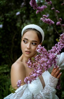 Beyaz elbiseli gelin ve başında taç çiçek açan ağaçların arasında. Esmer kız, saçı topuz gibi. Çiçek açan pembe sakura 'nın arasında duruyor, pullu ve uzun kollu beyaz elbise, kız başka tarafa bakıyor.