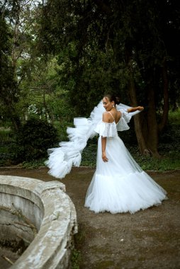 Uzun beyaz elbiseli gelin döner ve duvak atar. Duvak rüzgarda sallanıyor, esmer kız düz saçlı, düğümlenmiş. Kız gülüyor. Arkasındaki ağaçlar