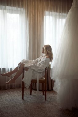 Güzel kız gelin, düğün sabahı otelde sandalyede oturur. Sarışın oturuyor ve düğünle ilgili rüyalar görüyor, beyaz cüppeli, düğün gününe hazırlanıyor, gelinliği yakınlarda.
