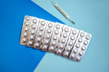 Gümüş kabarcıklı tabletler ve mavi arka planda bir termometre. Bir sürü kabarcık var, bir sırada yatıyorlar.