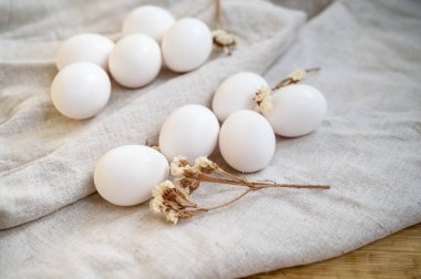 Beyaz tavuk yumurtaları masanın üzerinde doğal keten bir masa örtüsünün üzerinde yatar. Paskalya hazırlığı. Sağlıklı yiyecekler. Yüzeyde 10 parça var..