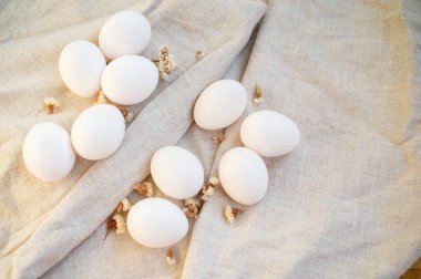Beyaz tavuk yumurtaları masanın üzerinde doğal keten bir masa örtüsünün üzerinde yatar. Paskalya hazırlığı. Sağlıklı yiyecekler. Yüzeyde 10 parça var. en üstteki görünüm. 