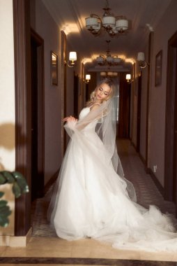 Güzel sarışın gelin otel lobisinde şık bir elbiseyle poz veriyor. Çıplak omuzları ve şık dalgalı saç stili ve makyajlı, dantel elbiseli zarif bir gelin. Trenli ve uzun peçeli giyin.