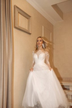 Güzel sarışın gelin otelin merdivenlerinden iniyor. Uzun bir gelinlik, dantel ve şifondan yapılmış bir korse. Dalgalı sarı saçları, güzel küpeleri var. Gülümsüyor.