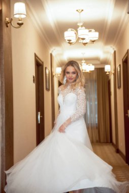 Otel koridorunda poz veren uzun beyaz elbiseli güzel sarışın gelin. Korseli ve omuzları açık şık bir elbise. Sarı saçlar bol ve şık bir stili var. Gülümsüyor, dönüyor.. 