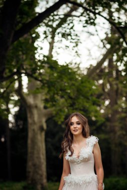 Çekici gelin, bahar parkında çiçek açan ağaçların arasında zarifçe poz veriyor. Zarafet, romantizm ve zamansız cazibe yayıyor. Avrupa tarzı korseli yumuşak pembe gelinlik. Etrafta büyük ağaçlar var. 