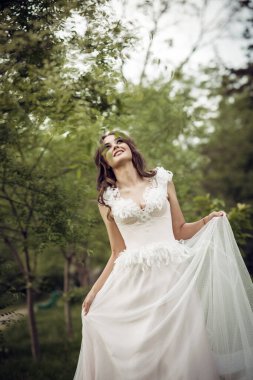 Çekici gelin, bahar parkında çiçek açan ağaçların arasında zarifçe poz veriyor. Zarafet, romantizm ve zamansız cazibe yayıyor. Avrupa tarzı korseli yumuşak pembe gelinlik. Gülüyor.. 