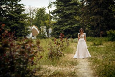 Çekici gelin, bahar parkında çiçek açan ağaçların arasında zarifçe poz veriyor. Zarafet, romantizm ve zamansız cazibe yayıyor. Avrupa tarzı korseli yumuşak pembe gelinlik. yatay