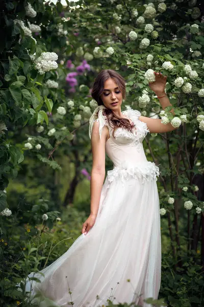 Çekici gelin, bahar parkında çiçek açan ağaçların arasında zarifçe poz veriyor. Zarafet, romantizm ve zamansız cazibe yayıyor. Avrupa tarzı korseli yumuşak pembe gelinlik. dikey