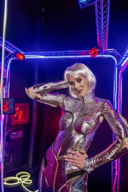 Siber robot gibi sarışın. Parlak gümüş renkli zırhlı kız. Sarışın, muhteşem makyajlı ve görüntüsü koyu tuşu ve renkli ışığı olan, siber uzayda poz veren. Ekranlar parlıyor