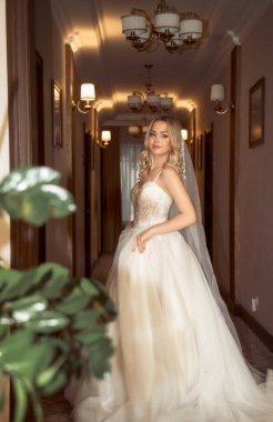 Güzel sarışın gelin otel lobisinde şık bir gelinlikle dikiliyor. Çıplak omuzları ve şık dalgalı saçı olan dantelli gelinlik içinde zarif bir gelin.