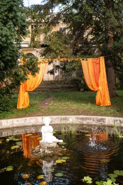 19. yüzyılda suda oturan beyaz bir melek şeklinde bir çeşme. Arkasında turuncu perdelerden yapılmış bir fotoğraf bölgesi var. Çevrelerinde yeşil ağaçlar var. Nilüferler çeşmede yetişir.