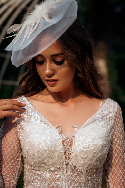 portrait of a young beautiful bride in a white dress and a white hat. white hat with a veil in a vintage style. in a spring park on a wedding day, a bright brunette in a stylish dress, a dress with a