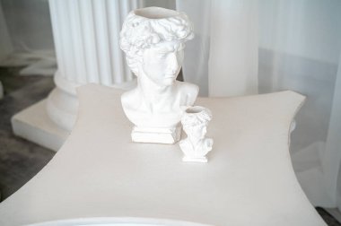 Antik ve Yunan tarzı antika heykeller için fotoğraf çekilecek bir yer. Masanın üzerinde iki alçı heykel duruyor. beyaz şifon kumaş ve kolonların arkasında