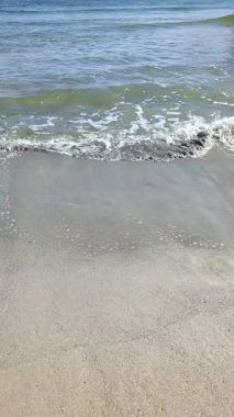 Açık havada küçük dalgalarla deniz kumlu sahilin durağan manzarası. Okyanus üzerinde ufuk çizgisi olan, açık mavi gökyüzü olan bir arka plan. Sakin, rahatlatıcı güneşli havanın ekran koruyucusu.