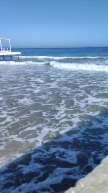 Açık bir günde küçük dalgalarla deniz kumsalının durağan manzarası. Okyanus üzerinde ufuk çizgisi olan, açık mavi gökyüzü olan bir arka plan. Kumlu kıyılarda hafif dalgalar