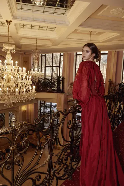 Lüks bir otel odasının arka planında kırmızı, uzun bir elbise giymiş bir model. İçinde kristal avizeler, aynalar ve içeride sahte elementler var. Otel lobisinde zarif genç bir bayan..