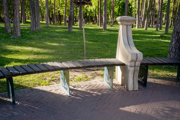 Parkta taş elementleri olan minimalist ahşap bir bank. Sessiz bir parktaki yemyeşil alanların arasında. Konforlu dinlenme alanı. Rahatlayacak yer